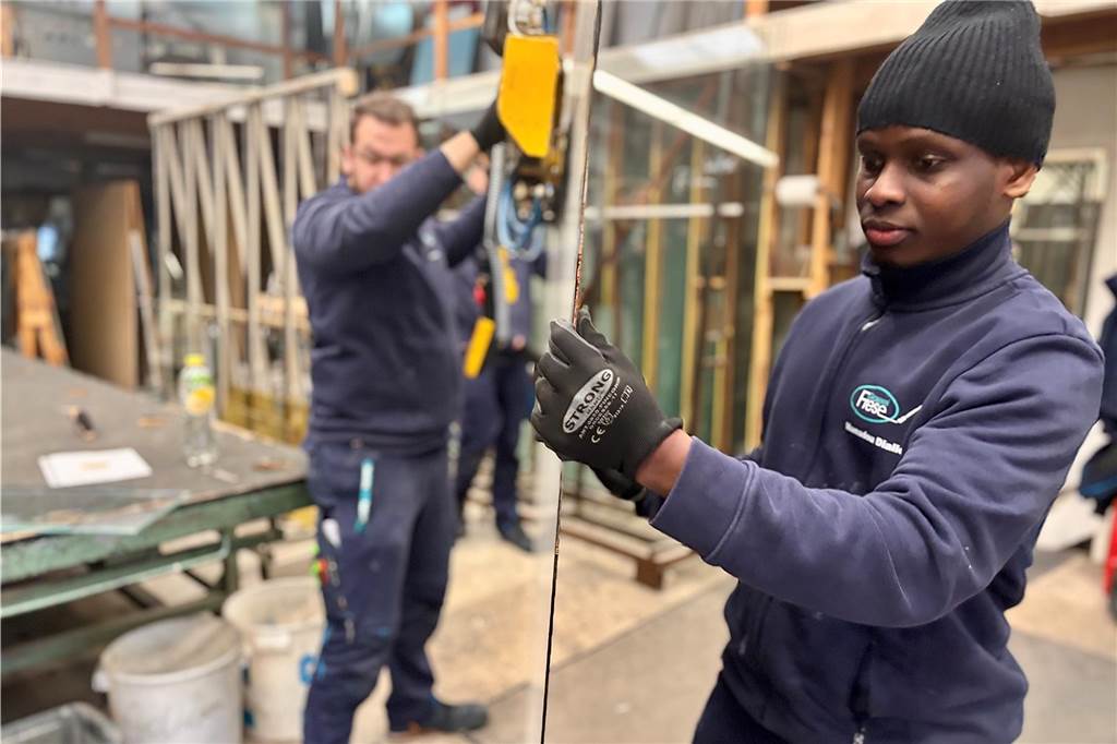 Mamadou Diallo führt mithilfe einer Maschine eine große Glasscheibe durch die Produktionshalle.