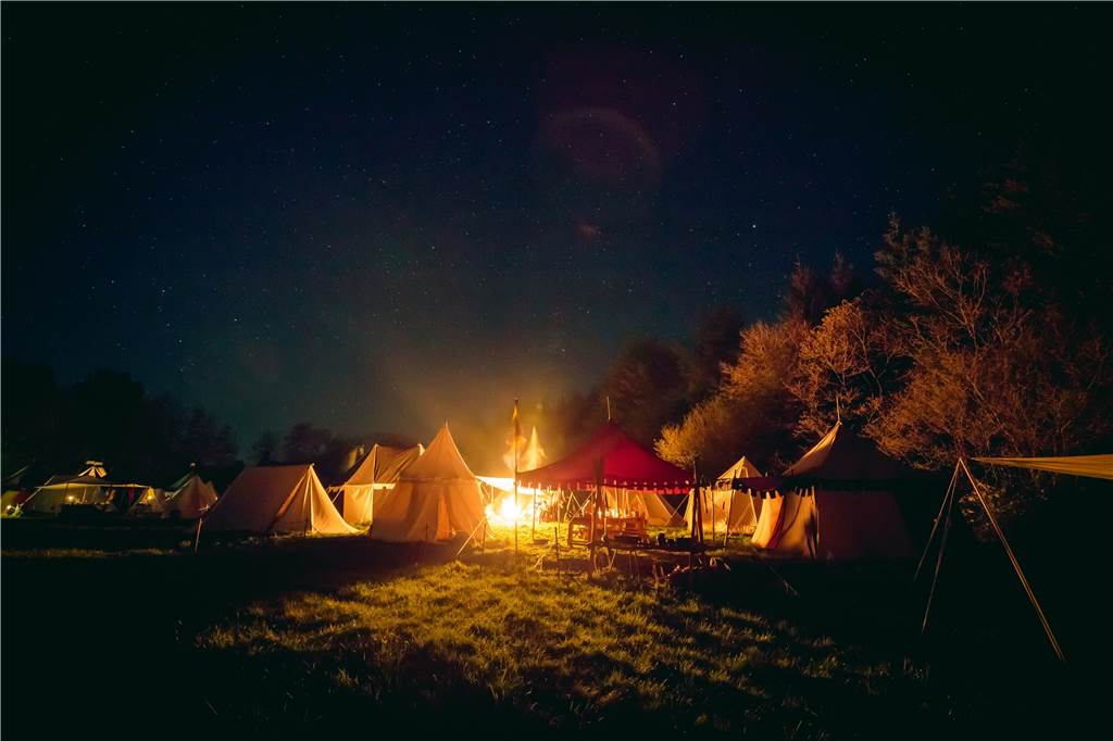 zelte und feuer auf einer großen wiese bei nacht