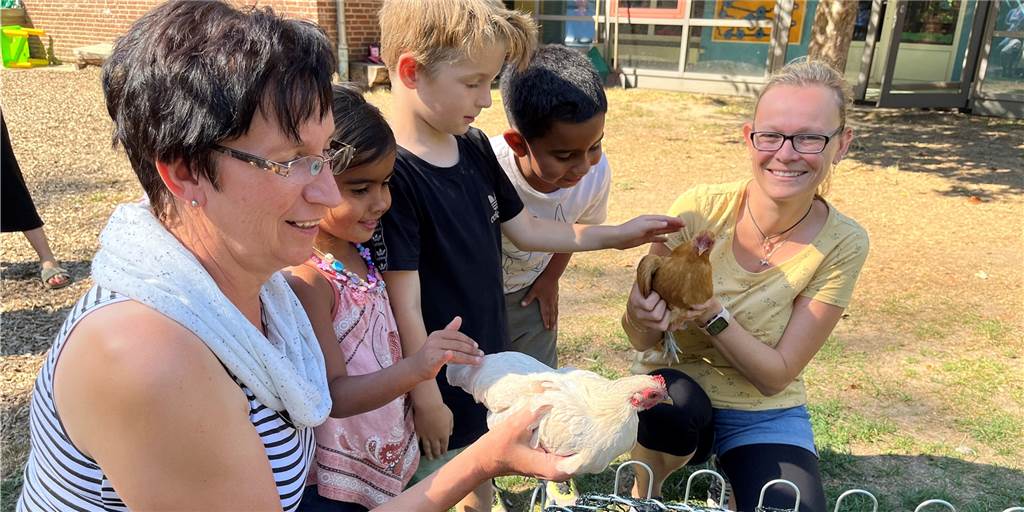 Ein Hahn, vier Hennen und das erste Ei - Kinder lieben ihre Hühnerschar Maria Bennemann (l.) und Jennifer Hollan (r.) vom Kindergarten Heilig Kreuz halten Schneeflöckchen und Goldie so, dass die Kinder die Hühner streicheln können. Der Hühnerhof in der Einrichtung hat seine besondere Geschichte.