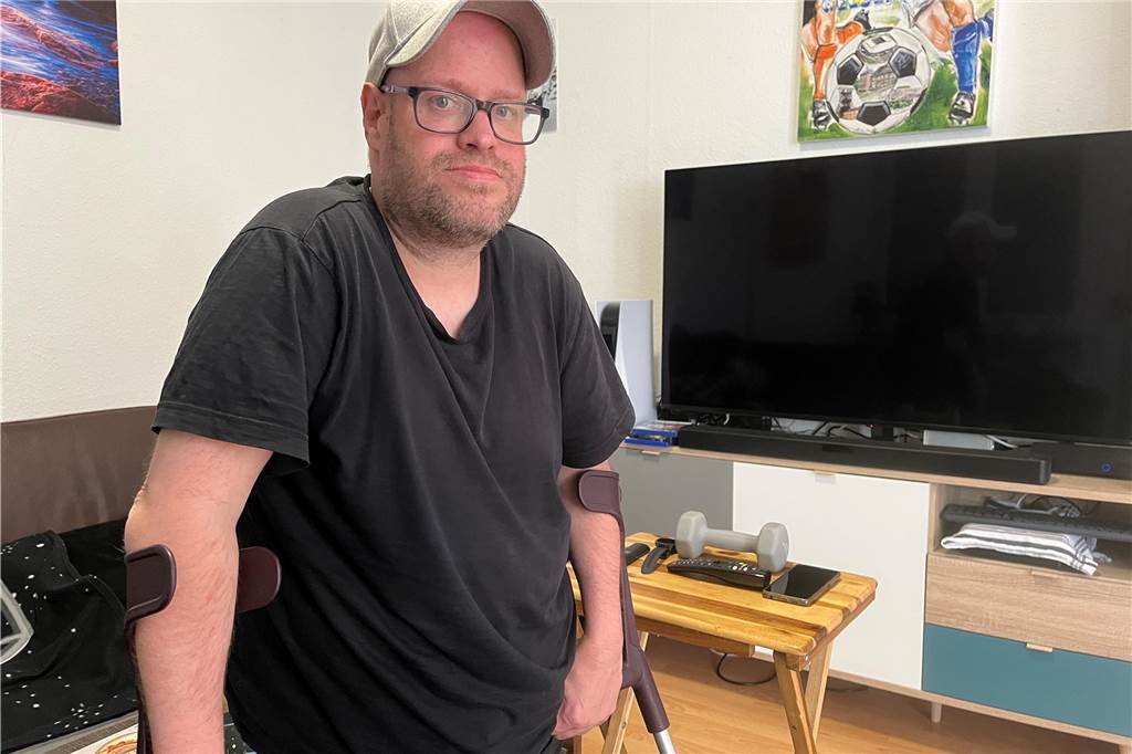 Mann steht an Krücken in seinem Wohnzimmer