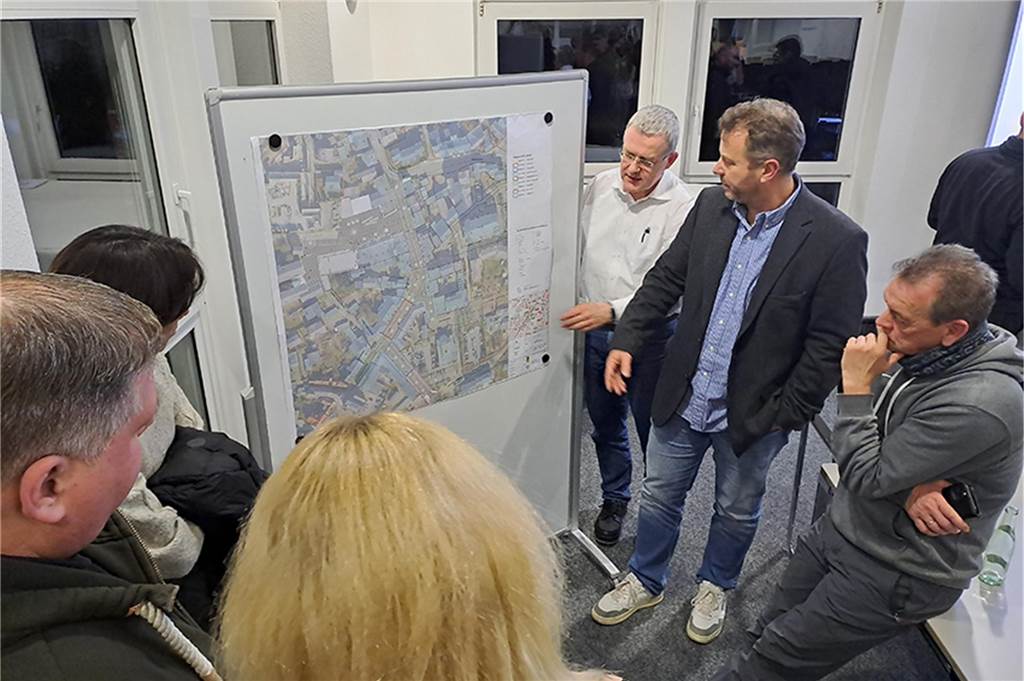 Markus Klaverkamp steht mit Bürgern vor einer Tafel, auf der ein Lageplan des Ortskerns von Ascheberg aufgehangen wurde.