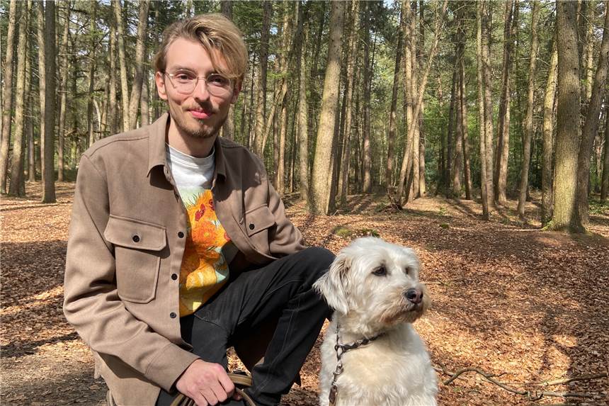 Wie sieht’s denn aus, Maximilian Großer: Hoodie oder Hemd, Buch oder Film? Maximilian Großer, Landtagskandidat der Grünen, hockt neben einem Hund in einem Wald.