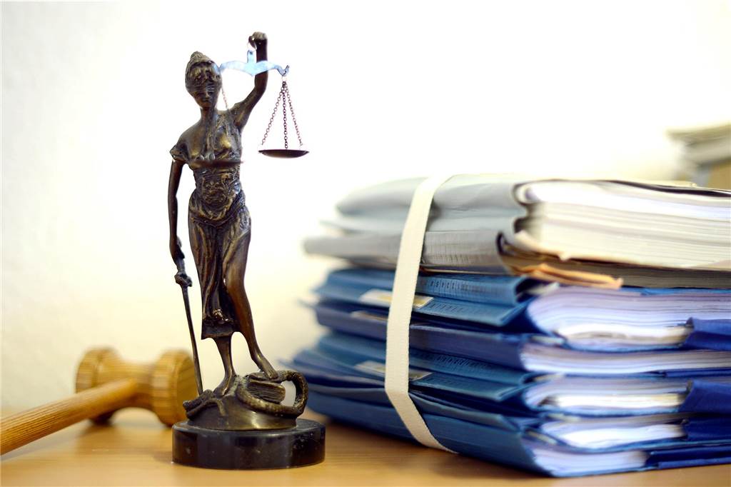 Die Justitia steht neben einem Stapel von Akten. 