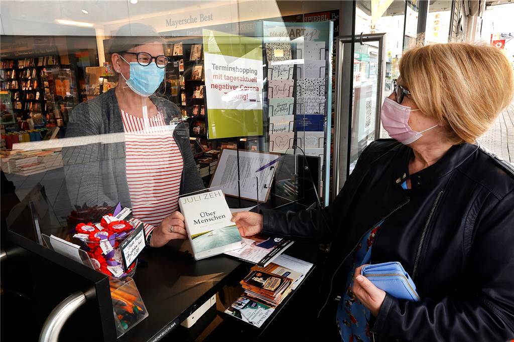 Meike Westermann (l), Filialleiterin der Mayerschen Buchhandlung, hat am Montag den Aushang im Schaufenster verändert. Der Schnelltest ist nicht mehr notwendig. 