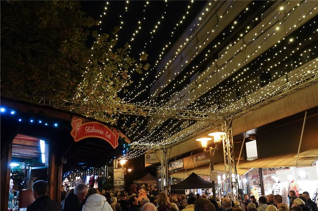 Glühwein, Mandeln und 3G: Die ersten Weihnachtsmärkte in NRW öffnen wieder Menschen laufen unter einer Lichterkette über den Weihnachtsmarkt in Essen. Der Markt im Stadtteil Steele hat am Donnerstag eröffnet.