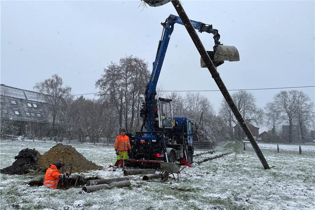 Mit dem Bagger heben die Arbeiter den Mast in das Loch. Mit Balken wird er fest verankert.