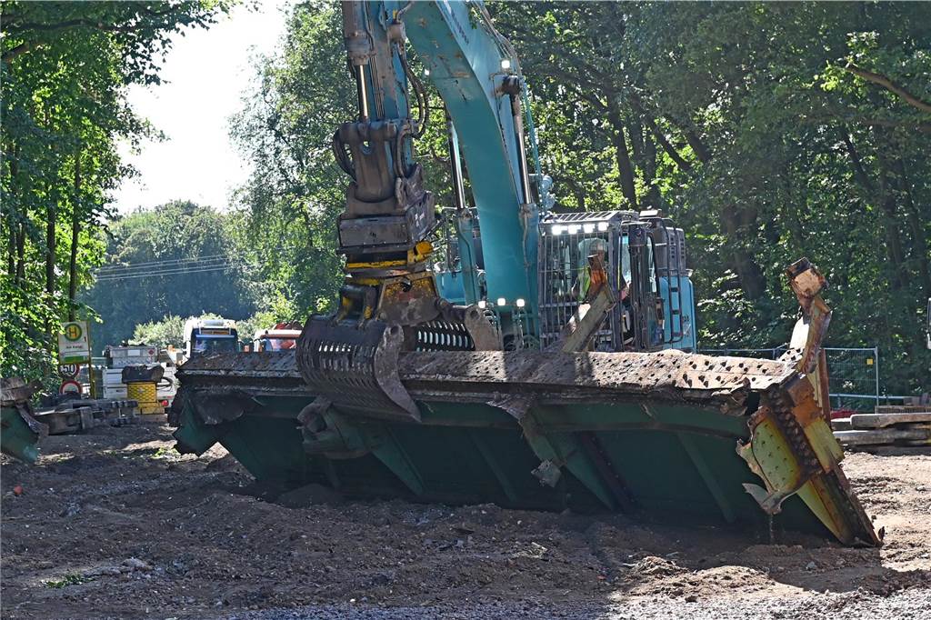 Mit einem Bagger werden die demontierten Stahlteile der alten Brücke zerkleinert und abtransportiert.