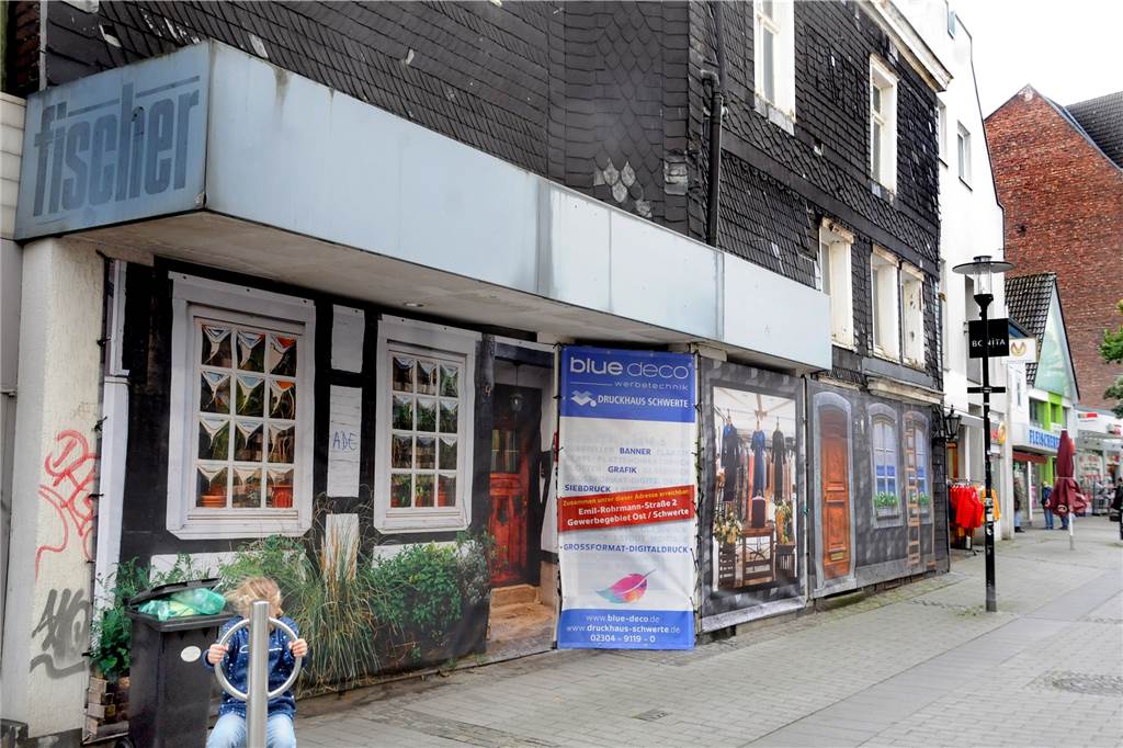 Mit einem neuem Transparent kaschiert haben Stadtmarketing und Stadtverwaltung die seit einer gefühlten Ewigkeit leerstehende Gaststätte „Alt Schwerte" an der Hüsingstraße. Dahinter verschwunden ist die Werbung für ein großes Ladenlokal, das bislang an dieser Stelle nicht gebaut worden ist.