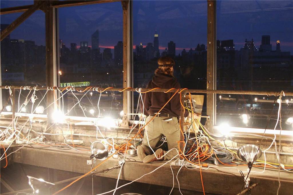 5 Dinge, die die Ausstellung „love/love“ über die Liebe lehrt Eine Frau kniet an einem Fenster, umgeben von Stromkabeln und Lichtern