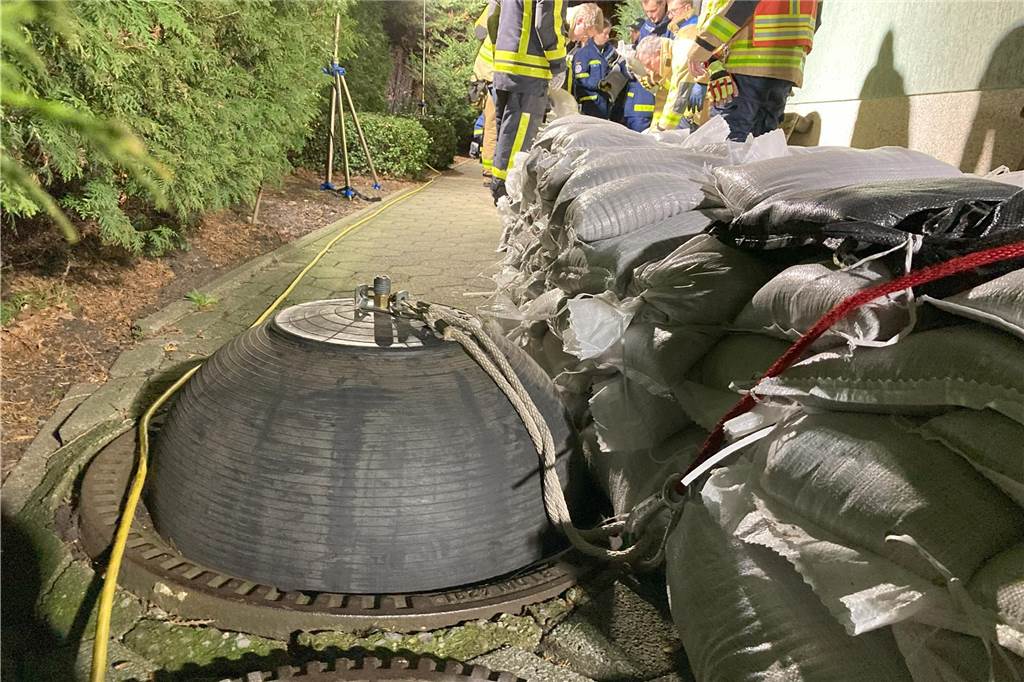 Feuerwehr und THW sichern Haus mit Sandsäcken: Hochwasser bei Ehepaar In einem geöffneten Kanalisationsschacht klemmt eine aufgepumpte Blase aus Gummi. Rechts daneben türmen sich Sandsäcke.