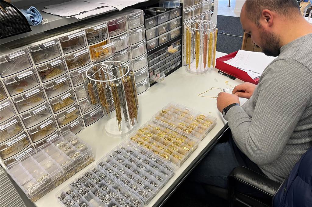 E-Commerce-Unternehmen eröffnet Ladengeschäft am Marktplatz Gökhan Yigit montiert eine Kette mit verschiedenen Buchstaben. Vor ihm liegen in vielen kleinen Fächern die Einzelteile aus Silber und vergoldetem Silber.