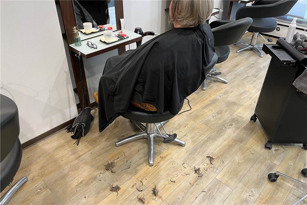 Haarbüschel reinigen die Meere: Haarmanufaktur Benson hilft der Umwelt Eine Kundin sitzt beim Friseur. Auf dem Boden liegen ihre abgeschnittenen Haare.