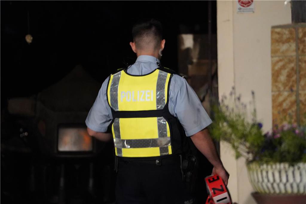 Garagenbrand in Groppenbruch greift auf Gartenhaus über Polizist mit Absperrband in der Hauseinfahrt.