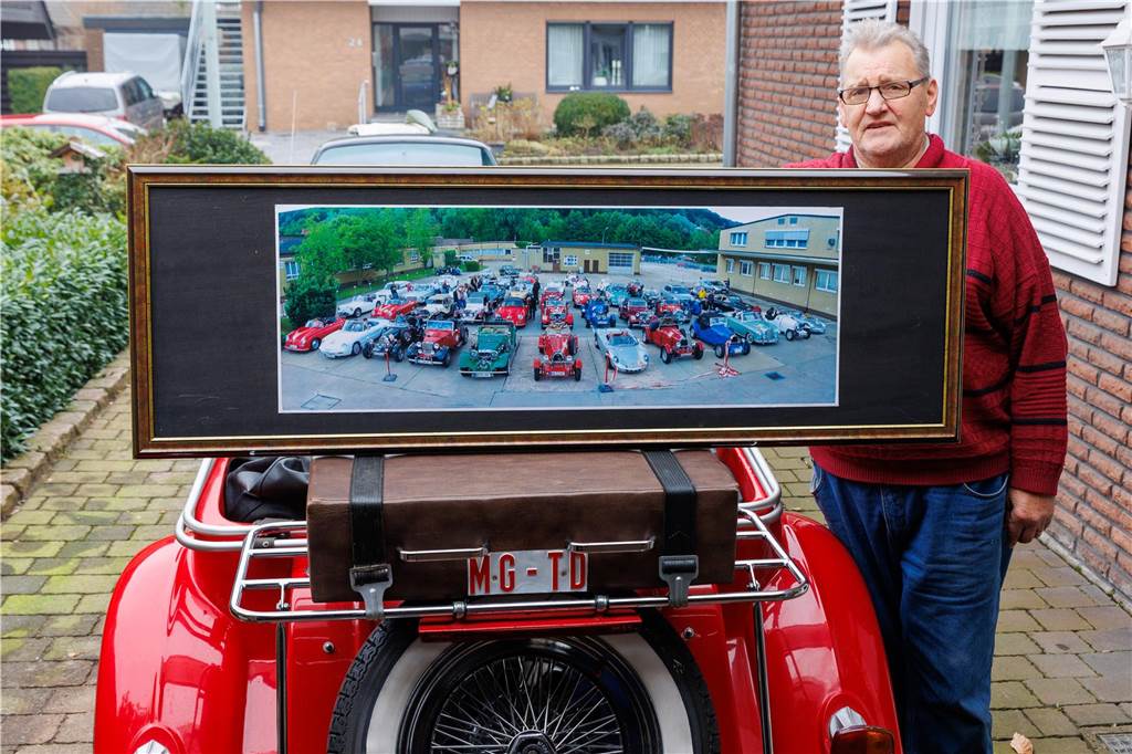 VW Käfer wird zum „Oldtimer“: Karl-Heinz Doods baut Kopie in Handarbeit Ein Mann hinter einem Bild und neben einem Auto.