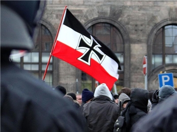 Neonazis schwenken eine Fahne hinter einer Polizeikette. Foto: Jan Woitas/Archiv