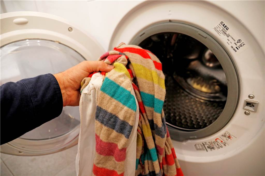Ein Mann legt Kleidung in eine Waschmaschine. 
