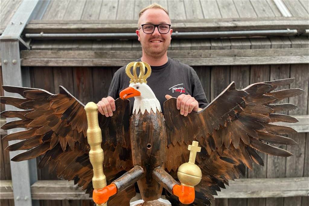 Niklas Aleff (25) baute den Rhader Schützenvogel in dritter Generation Mann steht vor einer Holzwand und hält einen Schützenvogel hoch.