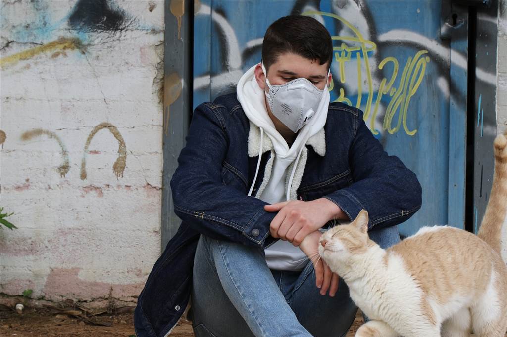 Corona-Sterberate zeigt: So unterschiedlich tötet das Virus in NRW-Städten Ein junger Mann sitzt mit einer Corona-Schutzmaske, streichelt eine Katze und schaut traurig vor sich hin.
