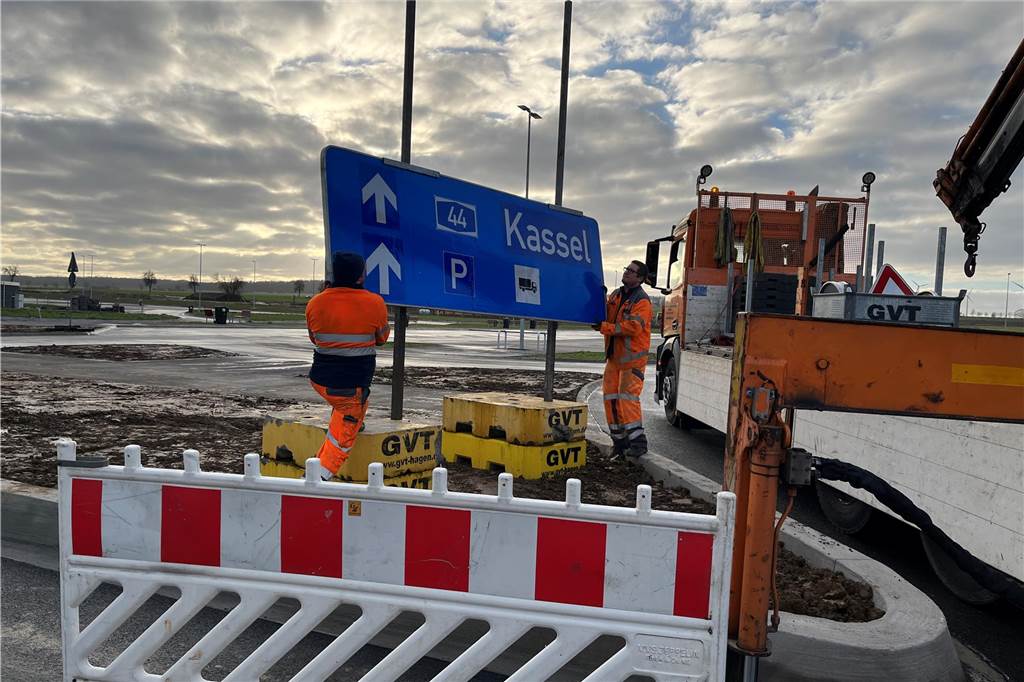 Ausbau für 12 Millionen Euro: A44-Rastplatz ist wieder freigegeben Zwei Bauarbeiter hängen ein Schild auf, das auf dem Rastplatz Haarstrang-Süd steht.