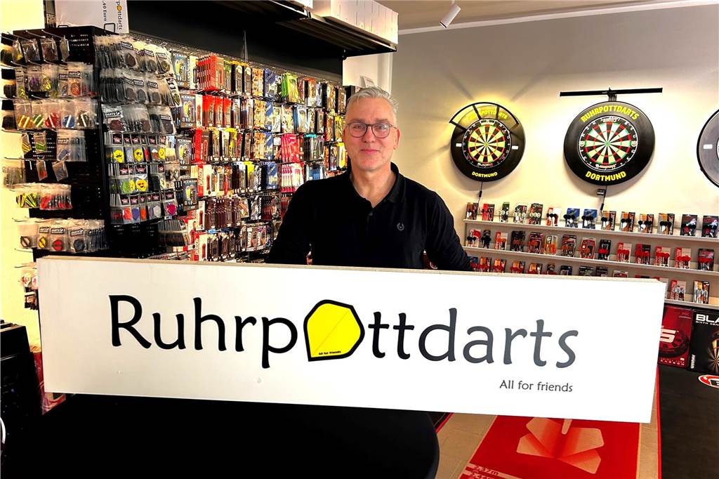Olaf Gebauer zeigt bei der Eröffnung seines Geschäfts in Dortmund-Aplerbeck ein Schild mit dem Namen "Ruhrpottdarts".