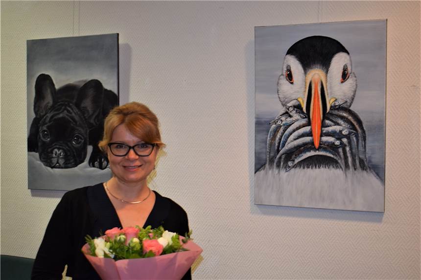 Olga Pelster vor ihrem Bild „Versorger“, das einen Papageientaucher zeigt. Links daneben: „Schön, dass du da bist“, das Portrait von einem kleinen Mops.