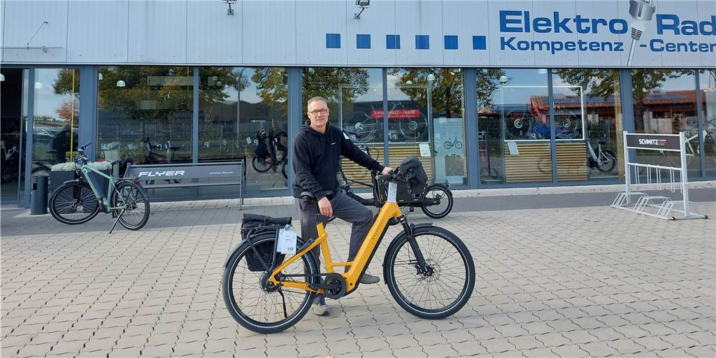 Immer mehr Unfälle mit Pedelecs - Fahrradexperte Oliver Trum weiß Rat Im Mittelpunkt steht ein Mann mit einem gelben Pedelec-Rad. Im Hintergrund sieht man ein Fahrradgeschäft. Links hinten steht noch ein grünes Fahrrad, rechts hinten ist ein Fahrradständer zu sehen.
