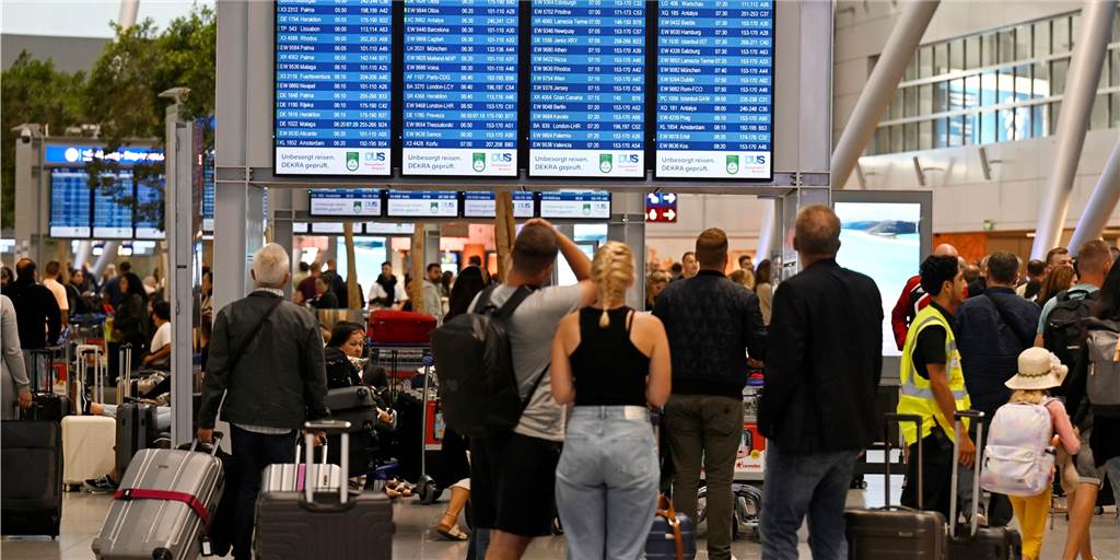 Flugtickets: Warum das Prinzip Vorkasse auf dem Prüfstand steht Passagiere stehen am Flughafen vor dem Flugplan.