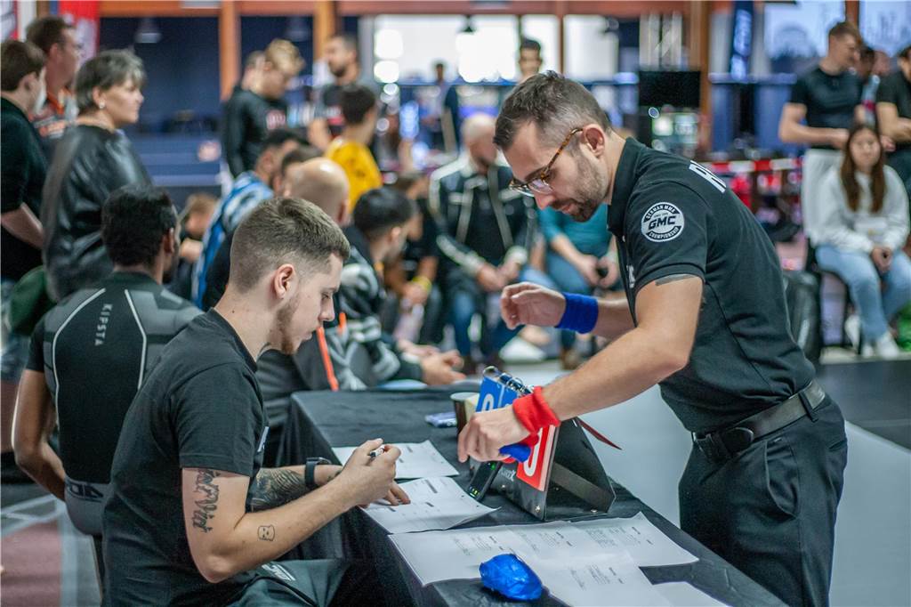 Mit Thorsten Legat in der Ringecke: Patrick Bork bestreitet Wrestling-Kampf Patrick Bork (r.) steht als Kampfrichter vor einem Pult und zeigt auf einen Zettel.