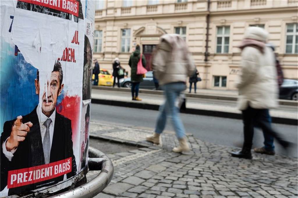 Ein leicht zerissenes Wahlplakat von Babis an einer Straßenecke, Passanten im Hintergrund.