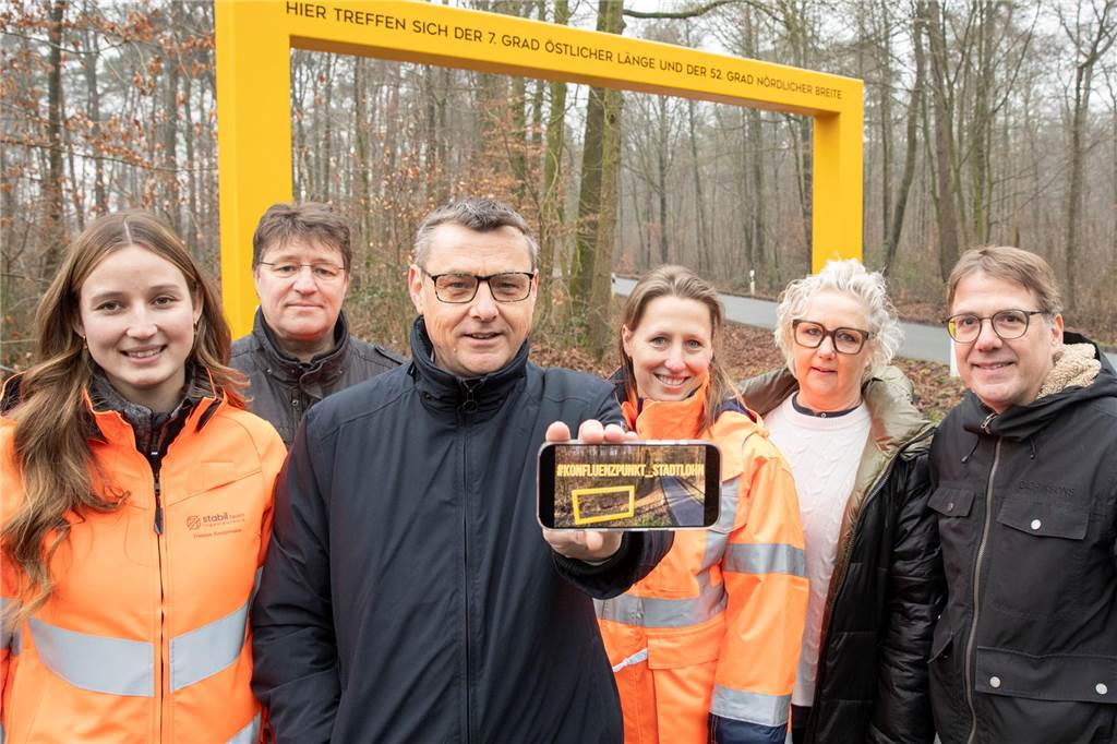 Bürgermeister Berthold Dittmann zeigt das Display eines Smartphones vor dem Bilderrahmen
