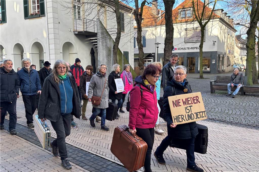 Teilnehmer laufen durch die Innenstadt. Einige halten Koffer und Schilder, welche zum Erinnern aufrufen. 