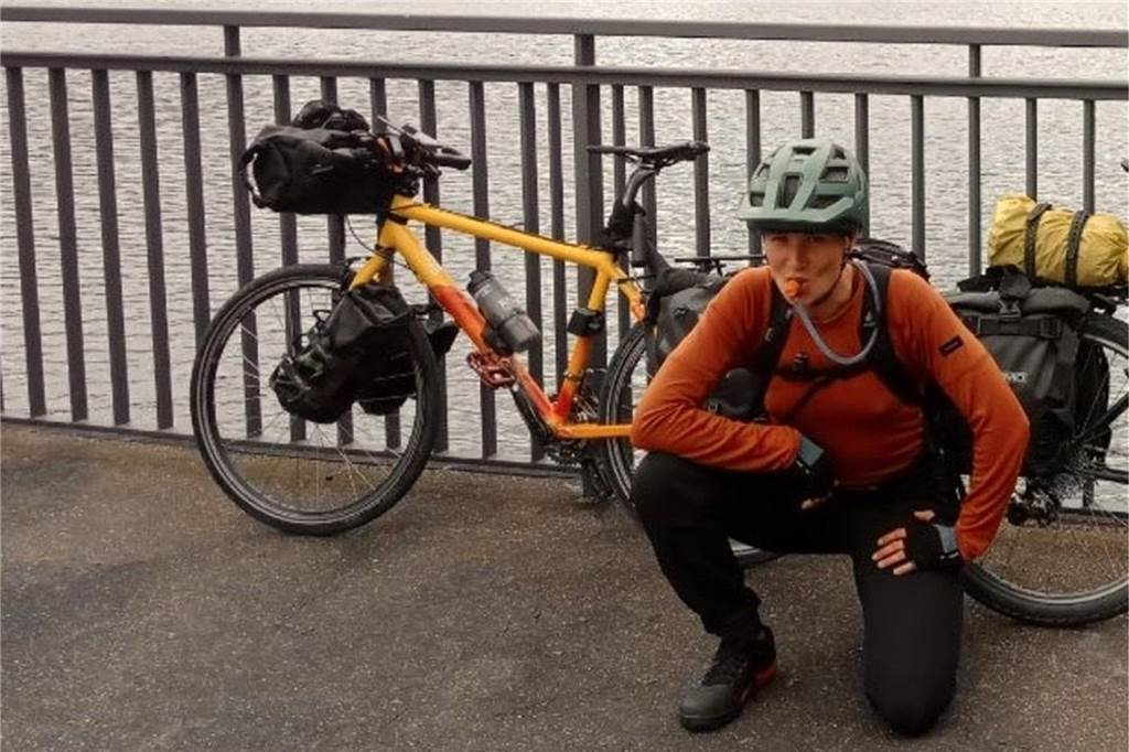 Pia kniet vor einer Brücke. An der Brücke lehnt ihr buntes Fahrrad.