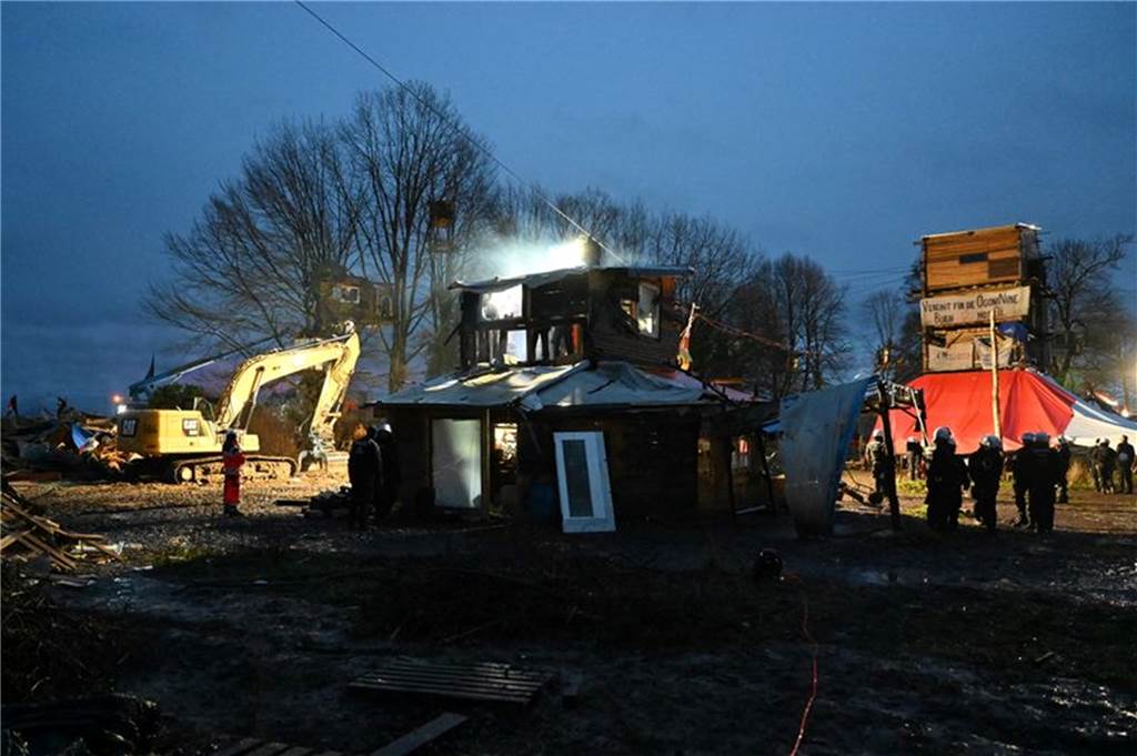 Lützerath-Räumung bis tief in die Nacht: Aktivisten betonieren sich ein Polizisten im von Klimaaktivisten besetzten Braunkohleort Lützerath vor einer Holzhütte.