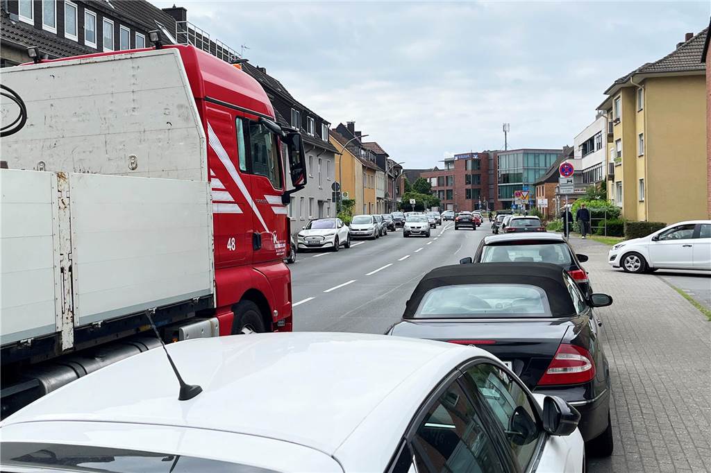 Eine stark befahrene Straße, an der auf beiden Seiten Autos parken.
