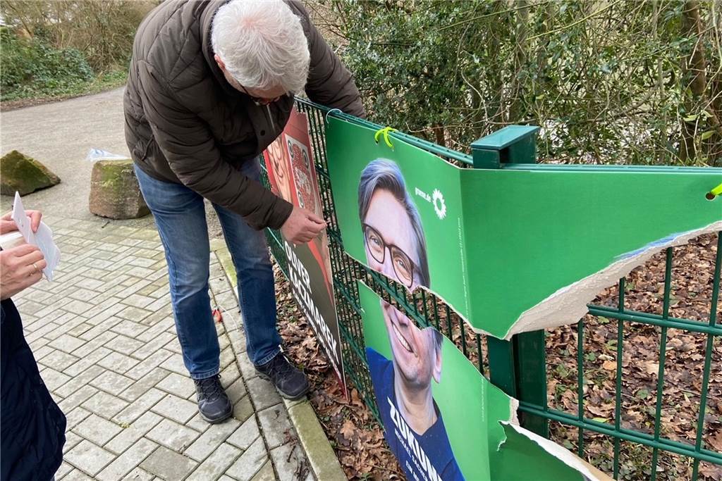 Ratsmitglied Uwe Gerken (SPD) repariert ein Plakat - zum dritten Mal innerhalb einer Woche. Das Grünen-Plakat daneben lässt sich nicht mehr retten.