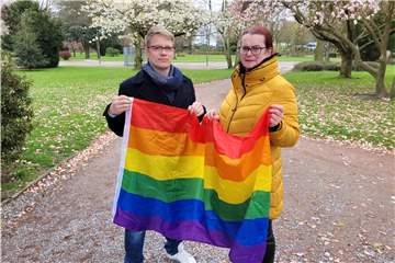 Rita Nowak und Daniel Petzoldt stehen mit einer Regenbogenflagge im Stadtpark.