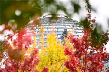 Rot-gelb-grün herbstlich verfärbte Blätter sind an Bäumen vor der Reichstagskuppel zu sehen. 