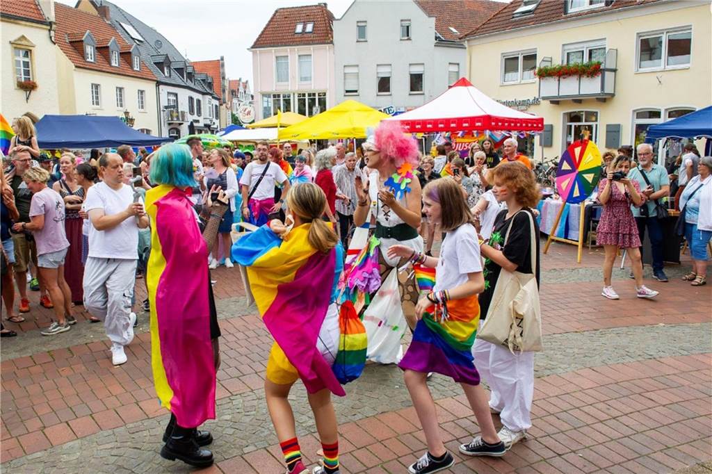 Kleemann zur Kritik am CSD: „Kirche wird ihrem eigenen Geist gerecht“ Menschen tanzen auf dem Marktplatz, einige haben sich eine Regenbogenfahne umgelegt.