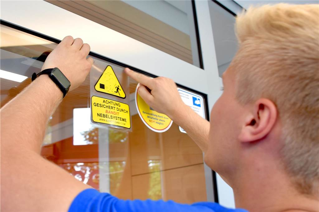 Volksbank im dichten Nebel: Testlauf gegen neue Sprengung von Geldautomaten Ein Mitarbeiter bringt Hinweisschilder auf die Nebelanlage in Wüllen an