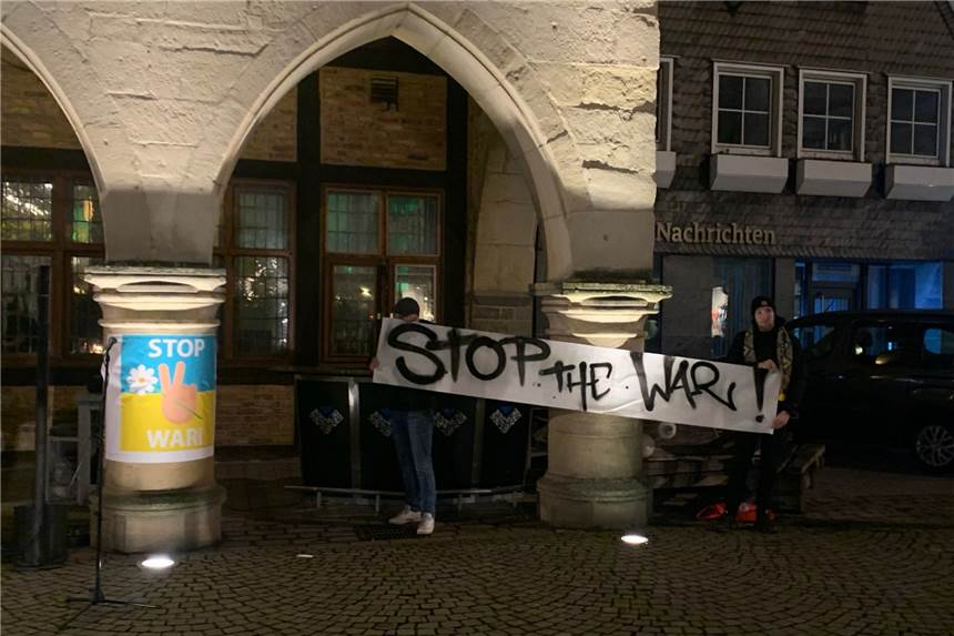 Zeichen für den Frieden: Internationaler Club Werne ruft zur Kundgebung auf Der Werner Markplatz am Abend. Man sieht zwei Personen, die ein Banner in die Höhe halten. Darauf steht "Stop the war".