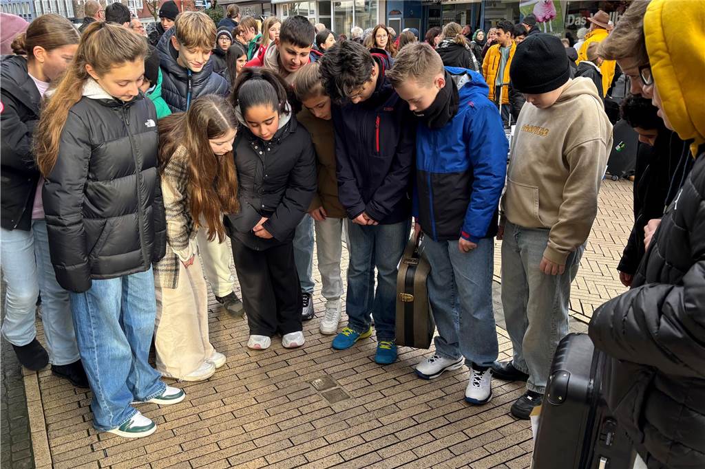 Schüler stehen im Halbkreis und sehen sich ein Monument im Boden in der Innenstadt an. 