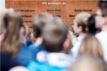 Schüler und Schülerinnen am Gymnasium stehen vor einer Gedenktafel. 