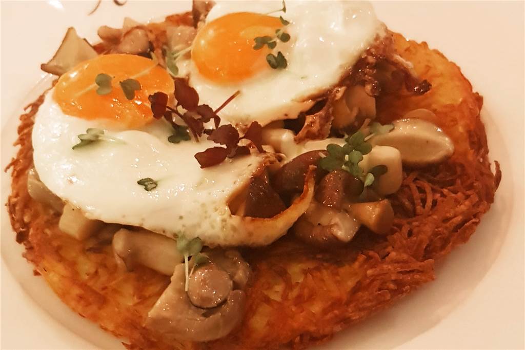 Schweizer Rösti mal tellergroß, dazu gebratene Pilze, Creme Fraiche und zwei Spiegeleier.