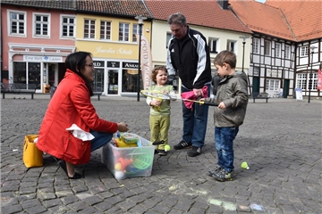 Seit einigen Tagen steht eine Spielzeugkiste auf dem Marktplatz. Dazu gehören auch Schwimmnudeln. Mara (2) und Jonas (4) spielen miteinander. Der Großvater von Mara, der sich "Opa Pöller" nennt, und Jonas' Mutter Nadia Koo schauen zu.