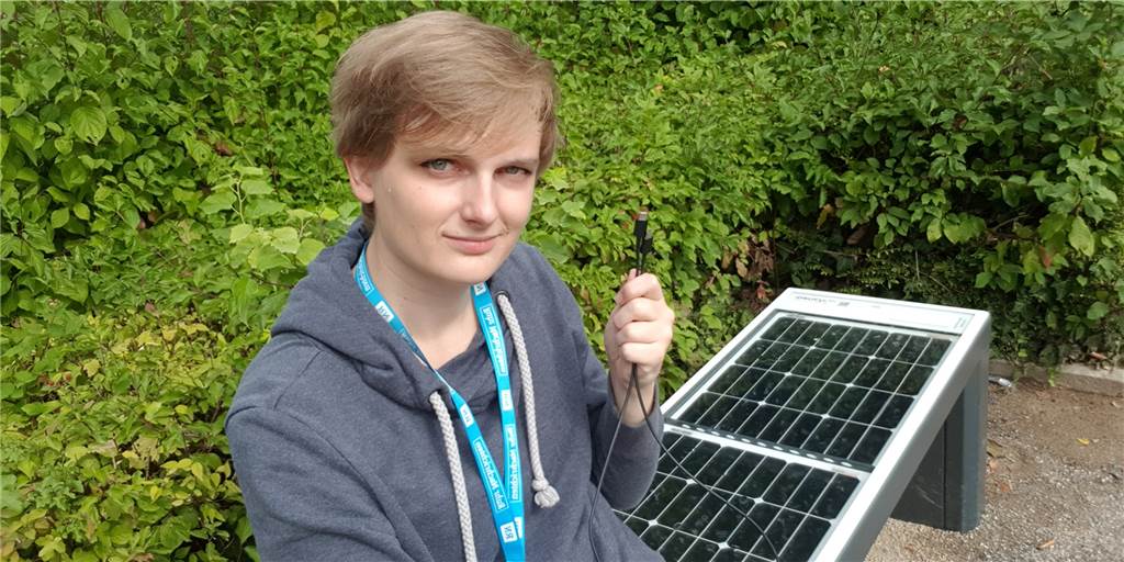 Solar-Sitzbank im Castroper Stadtgarten: Wir haben sie getestet Freie Mitarbeiterin der Ruhr Nachrichten sitzt auf der Solar-Sitzbank und hält dabei ein USB-C kabel in der Hand. Die Bank ist im Stadtgarten Castrop-Rauxel.