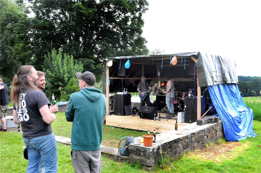 Woodstock-Feeling auf dem Gelände – obwohl „Esel Eckey“ seit Jahren geschlossen ist Selbstgezimmert wurde die Bühne zwischen den uralten Grundmauern eines längst verschwundenen Nebengebäudes von Esel Eckey. Als Schutz gegen den Nachmittagsregen - der ähnlich wie in Woodstock einsetzte - wurde sie eiligst mit Planen überdeckt.