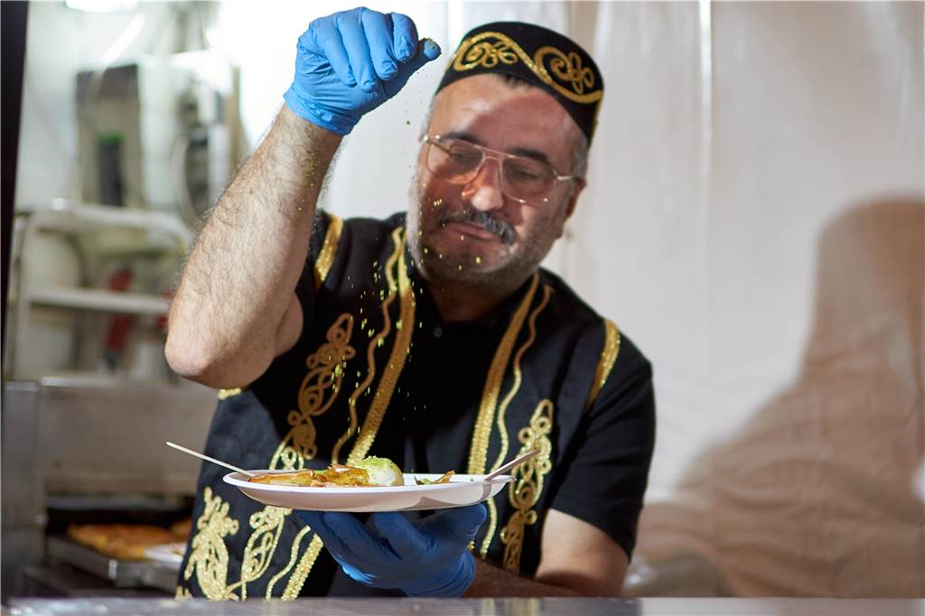 Sezai Cejlin streut noch ein bisschen geriebene Pistazie auf das Dessert, dann ist es servierfertig.