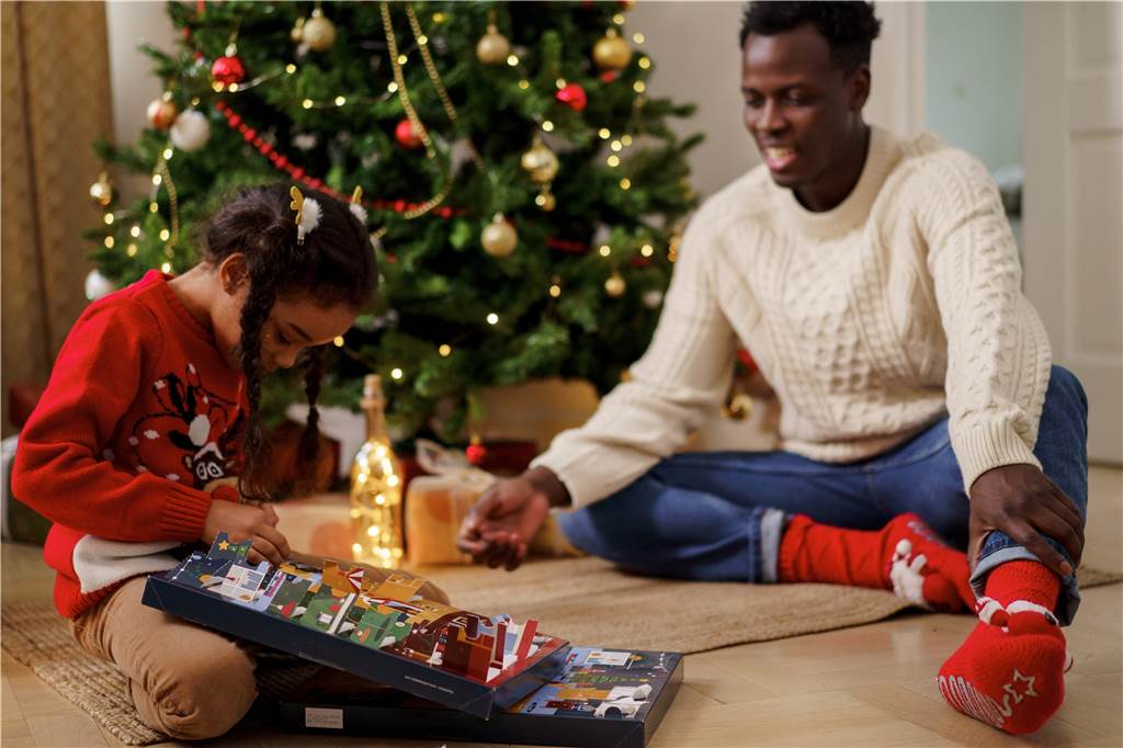 24 Glücksmomente: Schöne Ideen, um den Dezember-Alltag zu bestreiten papa schaut seiner tochter beim auspacken eines adventskalenders zu