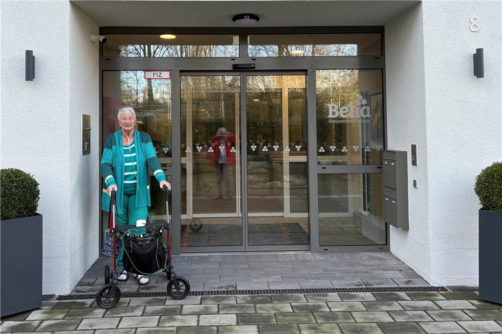 Uschi Pathmann steht mit ihrem Rollator vor dem Eingang eines Seniorenheims.
