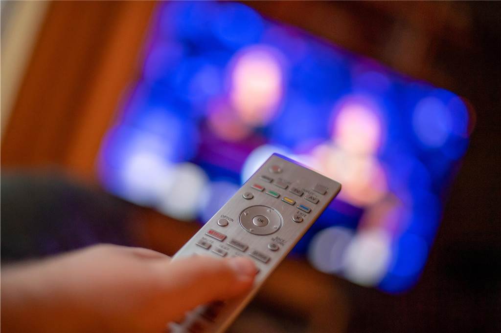 Eine Fernbedienung wird vor einem Fernseher gehalten.